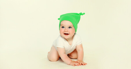 Happy baby in green hat playing on the floor on white studio background
