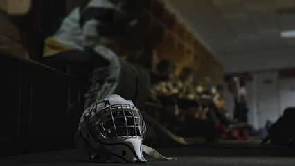 Helmet mask of Ice hockey goalkeeper goaltender is on floor inside locker room. Protective equipment gear in checkroom. Players sitting resting during break between periods intermission. Dressing room - Powered by Adobe