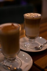 Vertical closeup shot of two cups of cappuccino with beautiful latte art on wooden table in a cafe.