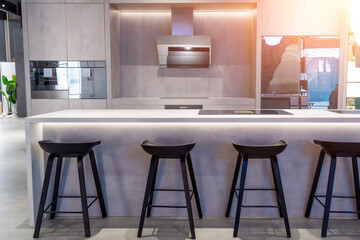 Kitchen in a new luxury home with a white island with a steel sink and induction hob, next to black chairs and stools