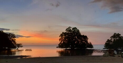 Landscape of trees reflecting on water with sunset orange sky on the horizon