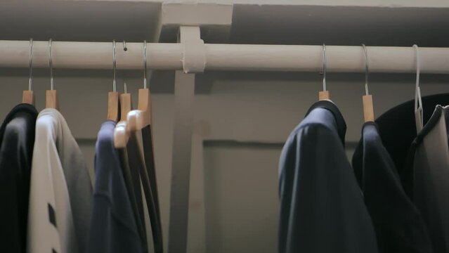 Clothing rack inside a closet. Man grabs a blue jacket inside wardrobe