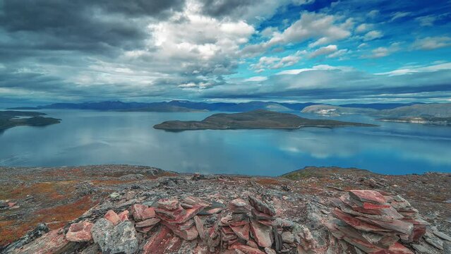 Whirling storm clouds backlit by the sun move above the serene fjord and mountains in the time-lapse video.