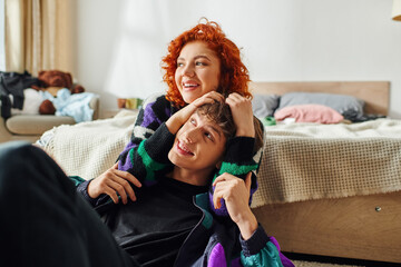 red haired alluring woman in casual stylish attire hugging her loving boyfriend while at home - obrazy, fototapety, plakaty