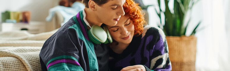 loving man with headphones hugging his cheerful red haired girlfriend while at home, banner