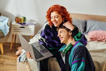 red haired jolly woman spending quality time with her joyous boyfriend while at laptop at home - obrazy, fototapety, plakaty