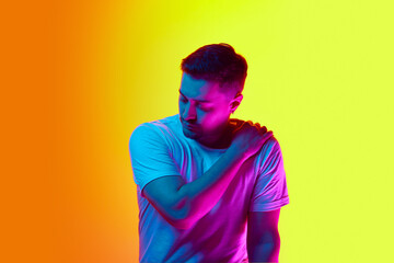 Portrait of young man posing in casual T-shirt in violet neon light against vibrant yellow studio...