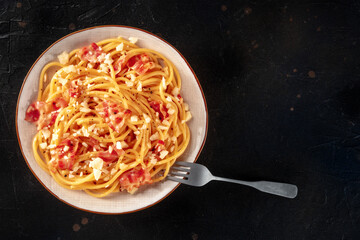 Carbonara pasta dish, traditional Italian spaghetti with pancetta and cheese, overhead flat lay shot with a fork and copy space, on a dark background