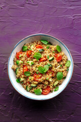 Quinoa tabbouleh salad in a bowl, a healthy dinner with tomatoes and mint, shot from above on a purple background