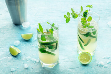 Mojito cocktail. Summer cold drink with lime, fresh mint, and ice. Cool beverage on a blue background with ingredients