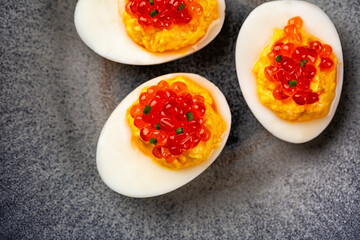 Top view of spiced deviled egg with salmon caviar on a grey plate.