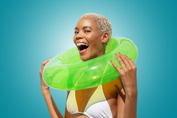 Happy laughing fun young woman holding green swim ring, African latin American woman isolated on blue background. Concept of a seaside vacation, shopping for a summer beach holiday or travel