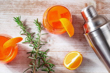 Orange cocktails with rosemary and a shaker, shot from the top on a wooden background