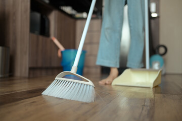 Young woman doing chores in kitchen sweeping floor with broom