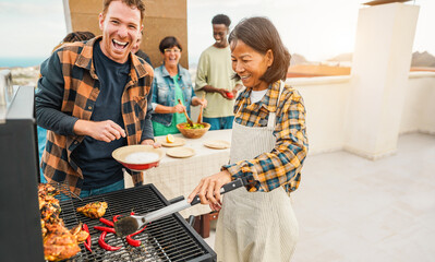 Happy multiracial friends having fun cooking healthy food with barbecue at rooftop house outdoor - Multigenerational people grilling chili and chicken during summer weekend meal