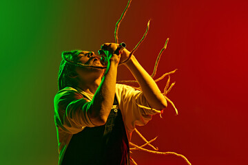 Dynamic image of artistic, soulful young man with dreadlocks, musician singing solo against...