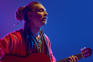 Captivating sight of man with dreadlocks pouring his soul into music, playing guitar against blue...