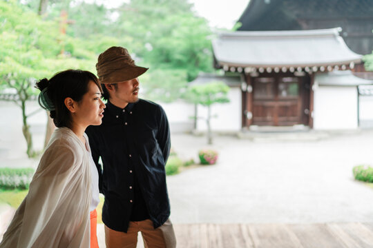 Japanese couple stands thoughtfully at a traditional site, with the serene temple grounds in soft focus behind