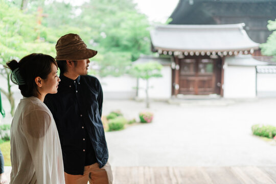 Japanese couple stands thoughtfully at a traditional site, with the serene temple grounds in soft focus behind