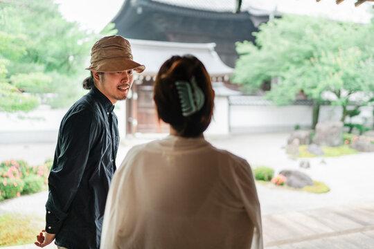 Japanese couple stands thoughtfully at a traditional site, with the serene temple grounds in soft focus behind