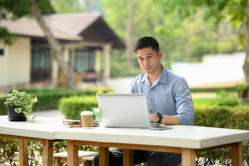 Adult businessman sitting at outdoor table and working on laptop computer
