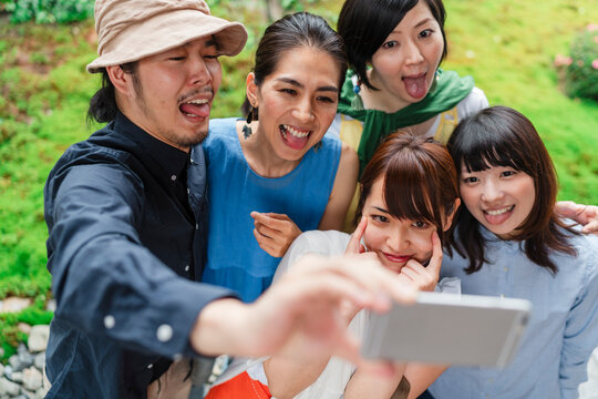 A group of five cheerful Japanese friends taking a selfie together outdoors, with a man holding the phone and everyone smiling broadly