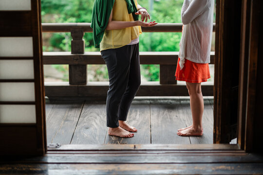 Two friends casually chat by a wooden railing, the lush backdrop hinting at a tranquil, natural setting