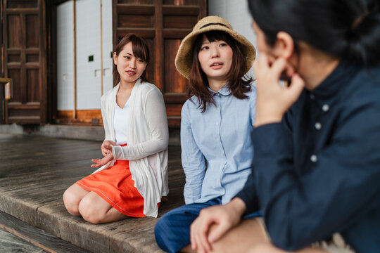 Three Japanese friends sitting on a porch engrossed in an intimate and serious discussion, in a traditional Japanese setting