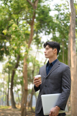 Portrait of handsome businessman holding paper cup of coffee standing in the public park