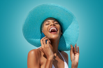 Happy woman portrait wearing blue sun hat and using mobile phone, isolated on turquoise bright...