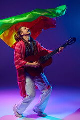 Expressive musician with dreadlocks lost in his guitar playing against t backdrop of colorful flag...