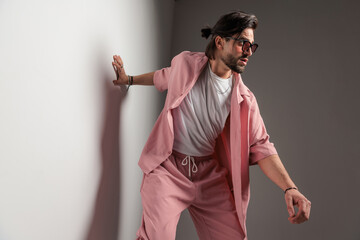 dynamic casual man in pink clothes with sunglasses holding hand on wall