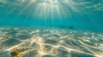 Underwater view of sunbeams filtering through crystal-clear water, illuminating a sandy ocean floor