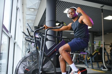 Athletic black man doing cardio workout on exercise bike in gym. Concept of sport and healthy lifestyle - obrazy, fototapety, plakaty