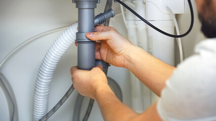 Close up of plumbers hands repairs plumbing pipes. Removing blockage clog in drain pipe. Replacement of plumbing pipes. Installing kitchen sink