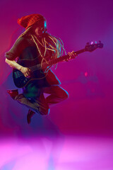 Dynamic image of artistic young man, musician playing guitar against pink background in neon with...