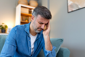 Closeup of man suffering from headache at home, touching his temples, copy space, blurred background. Migraine, headache, stress, tension problem, hangover concept