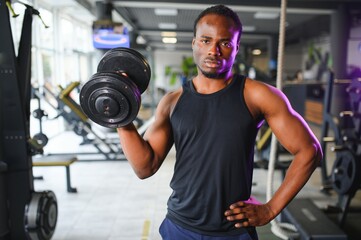 Young man strengthening biceps with dumbbell in gym