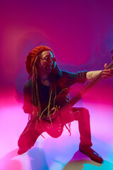 Atmospheric dynamic scene of guitarist with dreadlocks, male musician performing solo against pink...