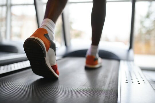 Back view of unrecognizable male legs running on treadmill in gym.