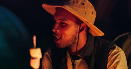 Camping, eating and face of man with marshmallow by fire at night on holiday, trip or vacation outdoor. Smile, nature and sweets with happy young hiker biting roasted or toasted food at campsite