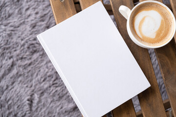 blank book mockup on wooden chair with cappuccino, pen and grey rug