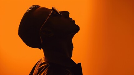 Silhouette of man in sunglasses against vibrant orange background, creating a striking and stylish image