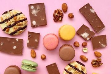 Pastel macarons, almond chocolate, peanut butter cookies and various nuts on bright pink background. Top view.