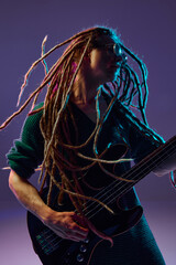Passionate performer with dreadlocks pouring his heart out through his guitar playing against dark...