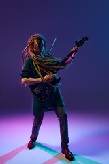Young man, musician, expressive guitarist with dreadlocks playing guitar, performing solo against...
