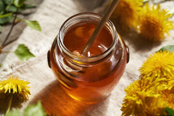 A jar of dandelion honey with fresh dandelion flowers