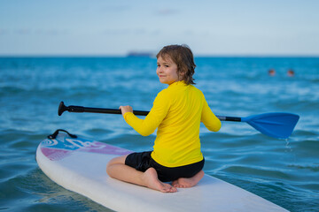 Boy swimming on stand up paddle board. Water sports, active lifestyle. Kid paddling on a paddleboard in the ocean. Child Paddle boarder. Summer Water sport, SUP surfing. Summer beach vacation.