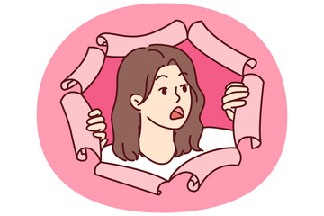 Shocked woman peeks out of hole in torn paper and looks away after seeing unexpected discount or promotional offer. Shocked girl feels fear and opens mouth wide hearing about stunning sale prices
