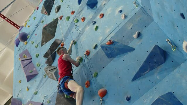 Low angle view of professional sportsman with disability abseiling off wall in climbing gym while finishing workout